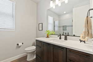 Full bathroom with wood finished floors, toilet, baseboards, a shower stall, and vanity