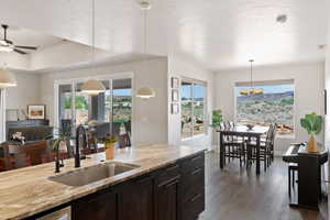 Kitchen with a sink, dark wood-style flooring, light stone counters, a chandelier, and pendant lighting