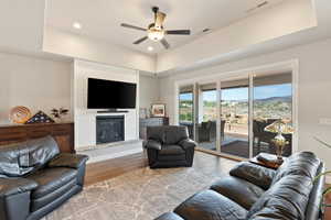 Living area featuring a ceiling fan, wood finished floors, a large fireplace, recessed lighting, and a tray ceiling