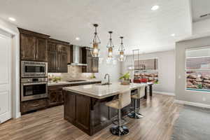 Kitchen featuring stainless steel appliances, wall chimney range hood, a sink, light wood-style floors, and light countertops