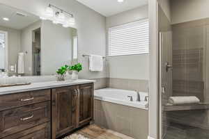 Full bathroom with a shower stall, a garden tub, vanity, wood finished floors, and recessed lighting