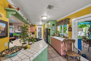 Kitchen with tile countertops, green cabinets, freestanding refrigerator, gas cooktop, and light tile patterned floors