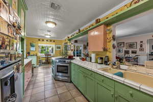 Kitchen featuring stainless steel gas range oven, fridge with ice dispenser, light tile patterned flooring, ornamental molding, and a peninsula