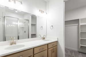 Full bath featuring a walk in closet, double vanity, a shower stall, and baseboards