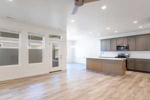 Kitchen with stainless steel appliances, tasteful backsplash, a center island with sink, ceiling fan, and light wood-style flooring