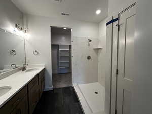Full bath with a tile shower, wood finished floors, double vanity, and a walk in closet