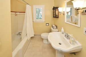 Full bathroom featuring toilet, a sink, baseboards, shower / bath combo, and tile patterned flooring