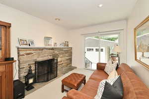 Carpeted living area with ornamental molding, a stone fireplace, and recessed lighting