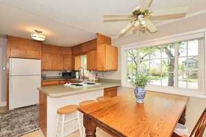 Kitchen featuring white appliances, a sink, a peninsula, a ceiling fan, and brown cabinets