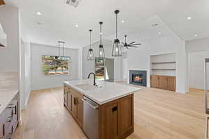 Kitchen with stainless steel dishwasher, a sink, a ceiling fan, brown cabinets, and a glass covered fireplace
