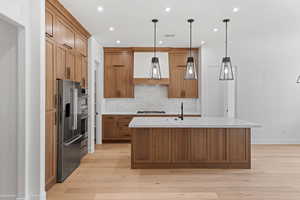 Kitchen with appliances with stainless steel finishes, extractor fan, tasteful backsplash, brown cabinetry, and light wood-style flooring