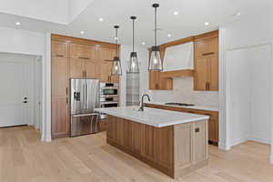 Kitchen with stainless steel appliances, custom exhaust hood, a sink, light wood-style flooring, and backsplash