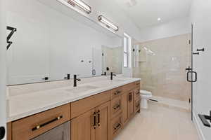 Bathroom featuring a shower stall, toilet, double vanity, and tile patterned floors