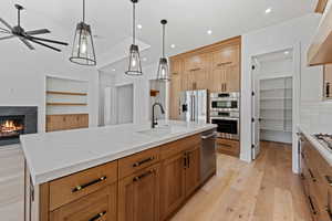 Kitchen with a sink, light wood finished floors, stainless steel appliances, a fireplace, and light stone counters