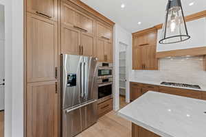Kitchen featuring stainless steel appliances, tasteful backsplash, light wood finished floors, light stone countertops, and hanging light fixtures