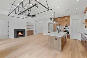 Kitchen with light wood-style floors, stainless steel appliances, a sink, a lit fireplace, and recessed lighting