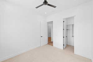 Unfurnished bedroom with light colored carpet, baseboards, a walk in closet, and ceiling fan