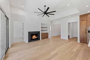 Unfurnished living room with recessed lighting, ceiling fan, light wood-type flooring, a fireplace, and built in shelves