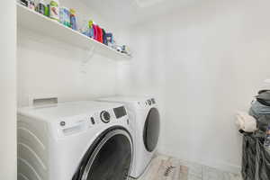 Clothes washing area featuring washing machine and clothes dryer, light marble finish flooring, and baseboards
