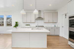 Kitchen featuring wall chimney range hood, light wood-style floors, recessed lighting, light countertops, and decorative backsplash