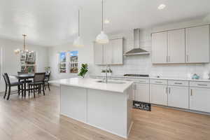 Kitchen with wall chimney exhaust hood, a sink, light countertops, light wood-type flooring, and backsplash