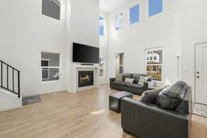 Living room with a towering ceiling, light wood-style flooring, a glass covered fireplace, stairway, and baseboards
