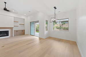 Unfurnished living room featuring a chandelier, light wood-type flooring, a glass covered fireplace, baseboards, and recessed lighting