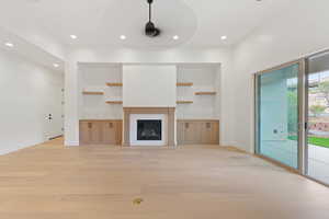 Unfurnished living room with light wood finished floors, recessed lighting, baseboards, built in shelves, and a glass covered fireplace