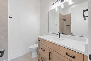 Bathroom with toilet, tiled shower, vanity, baseboards, and tile patterned floors