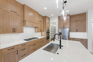 Kitchen with a sink, stainless steel appliances, pendant lighting, decorative backsplash, and light stone countertops