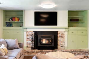 Living area with a textured ceiling, built in features, a brick fireplace, and wood finished floors