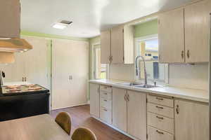 Kitchen with a sink, black range with electric cooktop, light countertops, under cabinet range hood, and light brown cabinetry