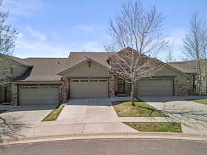 View of front facade with driveway, a shingled roof, a garage, and stone siding