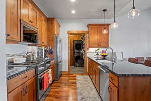 Kitchen featuring a sink, a peninsula, stainless steel appliances, stacked washer and clothes dryer, and decorative backsplash
