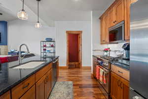 Kitchen with brown cabinets, a sink, dark wood-type flooring, appliances with stainless steel finishes, and decorative backsplash