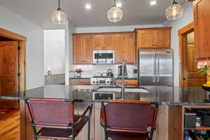 Kitchen featuring pendant lighting, a sink, wood finished floors, backsplash, and stainless steel appliances