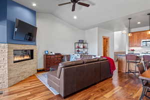 Living area featuring light wood finished floors, visible vents, a stone fireplace, ceiling fan, and vaulted ceiling