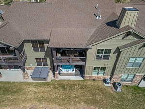 Rear view of house featuring board and batten siding, a patio area, stone siding, a lawn, and a shingled roof