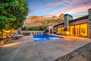 Pool at dusk featuring a mountain view, a patio, a pool with connected hot tub, and outdoor lounge area