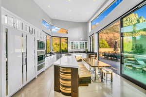 Kitchen featuring white fridge, white cabinetry, a towering ceiling, dark stone counters, and recessed lighting