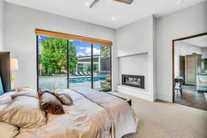 Carpeted bedroom featuring access to exterior, a glass covered fireplace, ceiling fan, and recessed lighting