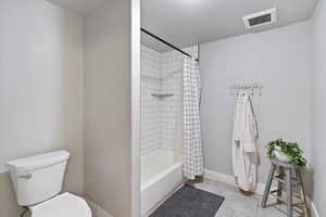 Separate room in the large bathroom featuring a tiled tub and shower combo, along with a toilet, offering privacy and functionality for a well-designed, multi-use space.
