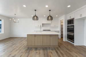 Kitchen with built in microwave, double oven, light countertops, recessed lighting, and light wood finished floors