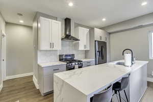Kitchen with stainless steel appliances, wall chimney range hood, a sink, baseboards, and light wood finished floors