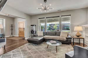 Living room featuring wood finished floors, a textured ceiling, a chandelier, baseboards, and visible vents