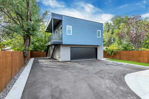 View of property exterior with stairs, an attached garage, fence, and asphalt driveway