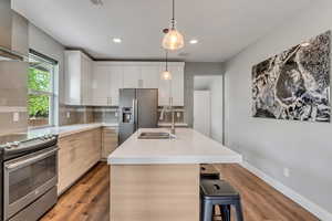 Kitchen featuring tasteful backsplash, wood finished floors, a sink, light countertops, and appliances with stainless steel finishes