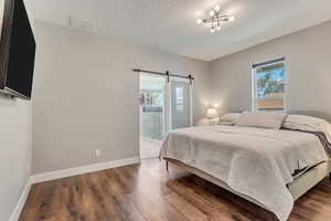 Bedroom featuring baseboards, a textured ceiling, a barn door, and dark wood-style flooring