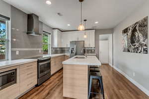 Kitchen featuring light countertops, wall chimney range hood, visible vents, a sink, and appliances with stainless steel finishes