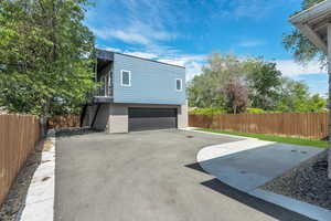 View of side of property featuring stairway, fence, stucco siding, an attached garage, and driveway